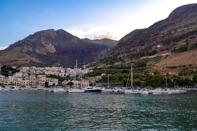 Sailboats moored on lake by mountains against sky