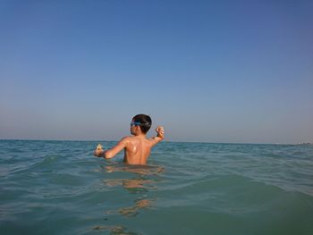 Full length of shirtless man in sea against clear sky