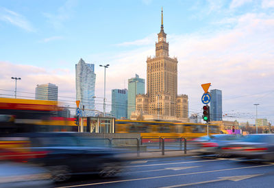 Cars on road by buildings against sky in city