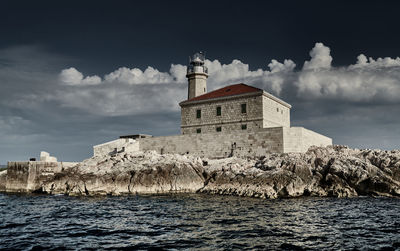 Lighthouse by sea and buildings against sky