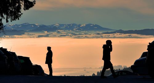 Silhouette people on landscape against sky during sunset