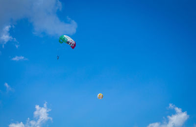 Low angle view of people paragliding against blue sky