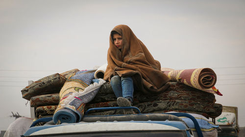 Boy looking away while sitting with blanket on truck 