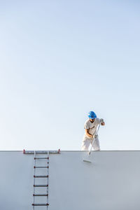 Unrecognizable young painter painting the facade of an apartment with a roller from the roof and the staircase on the side