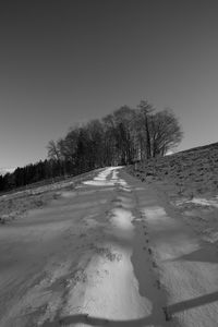 Tire tracks on snow covered field against clear sky