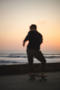 Rear view of silhouette man standing at beach against clear sky during sunset