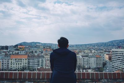 Rear view of man sitting towards cityscape against sky