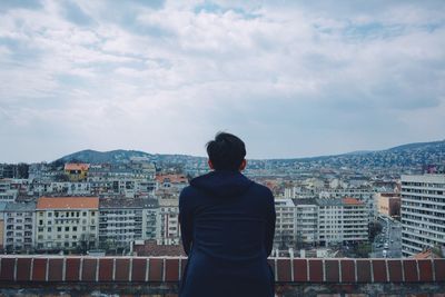 Rear view of man standing by cityscape against sky