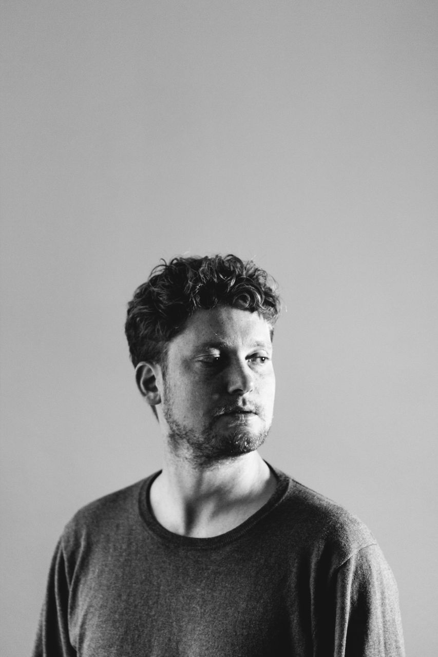 studio shot, front view, portrait, one person, indoors, casual clothing, copy space, young men, headshot, young adult, lifestyles, looking at camera, t-shirt, wall - building feature, men, beard, standing, looking, contemplation