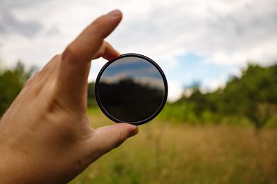 Cropped hand holding circular glass against trees