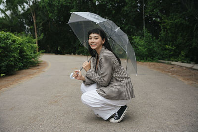 Young woman holding umbrella while standing on road