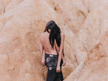 Rear view of woman standing on rock against wall