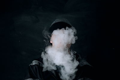 Close-up of man exhaling smoke against black background