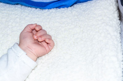 Cropped image of baby hand on bed