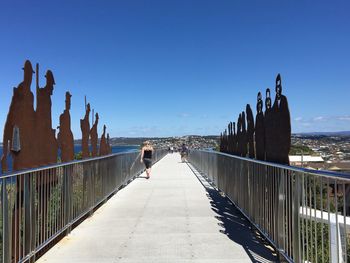 Rear view of man and woman on footbridge against clear sky