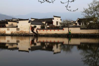 Reflection of houses and trees in water against clear sky
