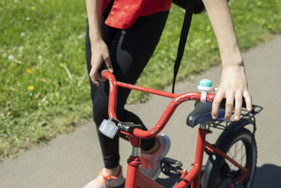 A teenager carries a bicycle holding onto the wheel. a girl rides her bike down the street. 