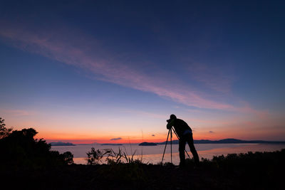 Silhouette man photographing sea against sky during sunset