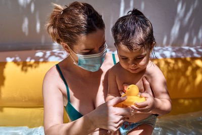 Young mother with a mask in an inflatable pool with her little daughter. safe holiday concept