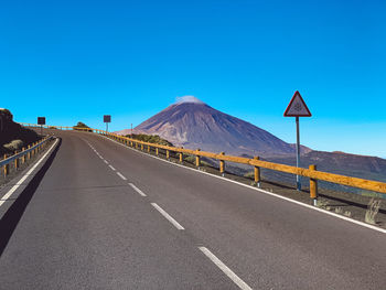 Road leading towards mountain against clear blue sky