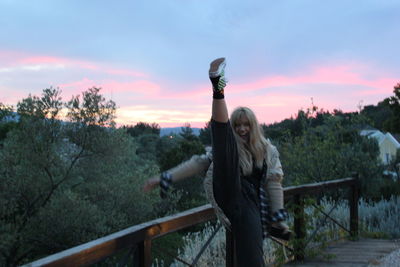 Woman standing by railing against sky during sunset