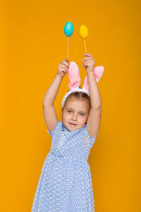 Rear view of girl holding balloon against yellow background