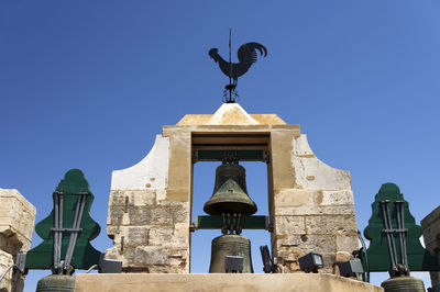 Low angle view of bell tower with weather vane against clear blue sky