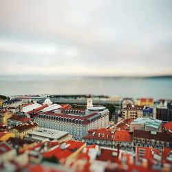 Tilt-shift image of buildings and sea against sky in city