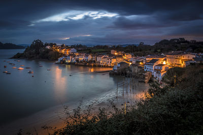 Illuminated buildings by sea against sky at sunset