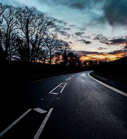 Road by silhouette trees against sky at sunset