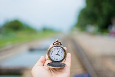 Close-up of hand holding clock against blurred background