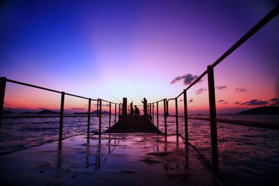 Silhouette men fishing in lake against dramatic sky during sunset