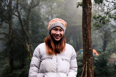 Portrait of smiling young woman standing against trees
