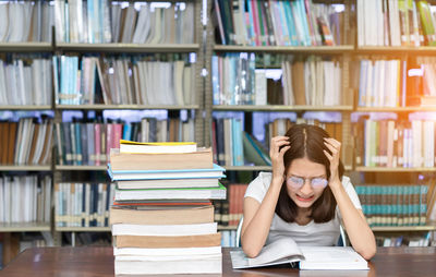 Young woman with head in hands studying at desk in library