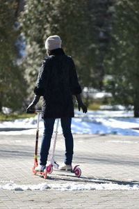 Rear view of woman riding push scooters on street during winter