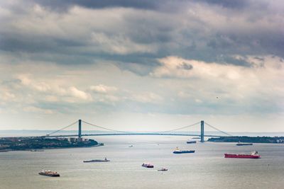 View of suspension bridge over sea against cloudy sky