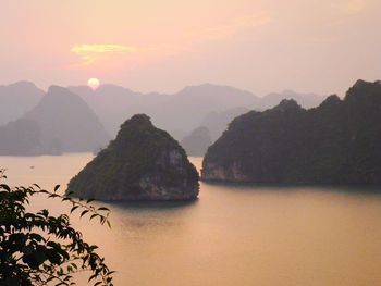 Scenic view of sea by mountains against sky during sunset