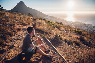 Man sitting on mountain against sky during sunset