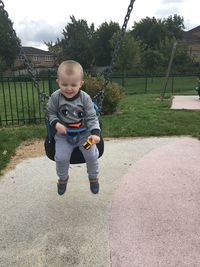 Playful baby boy sitting on swing at park