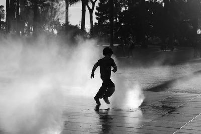 Full length of silhouette boy running amidst fountain in city