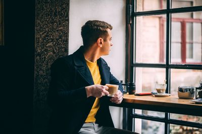 Full length of young man using mobile phone while sitting on table