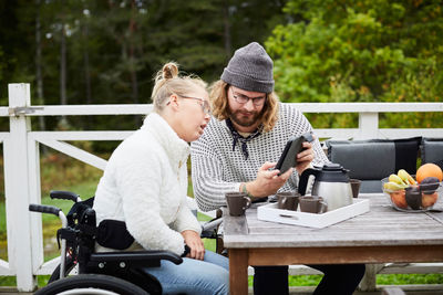 Young male caretaker using digital tablet with disabled woman in yard