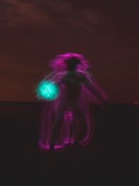 Blurred motion of woman standing against illuminated lights at night