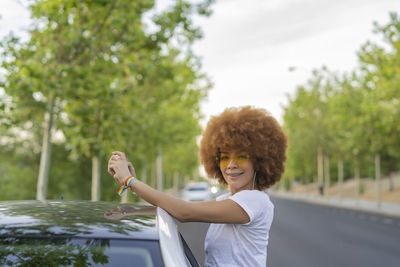 Woman with afro hair taking a photo with her smartphone next to her white car