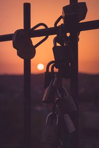 Close-up of padlocks on metal chain against sky during sunset