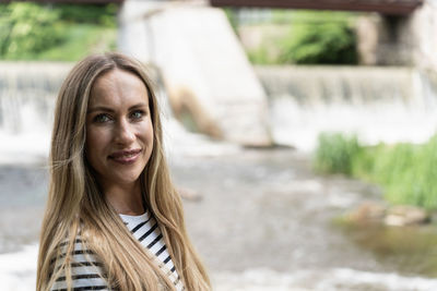 Focus on foreground on a smiling long-haired woman against the background of the river