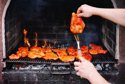 Midsection of person preparing meat on barbecue grill