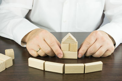 Midsection of man building house with wooden toy blocks at table