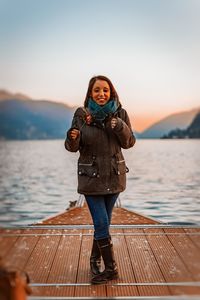 Portrait of woman standing on pier against lake during sunset
