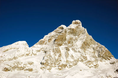 Low angle view of snowcapped mountain against clear blue sky